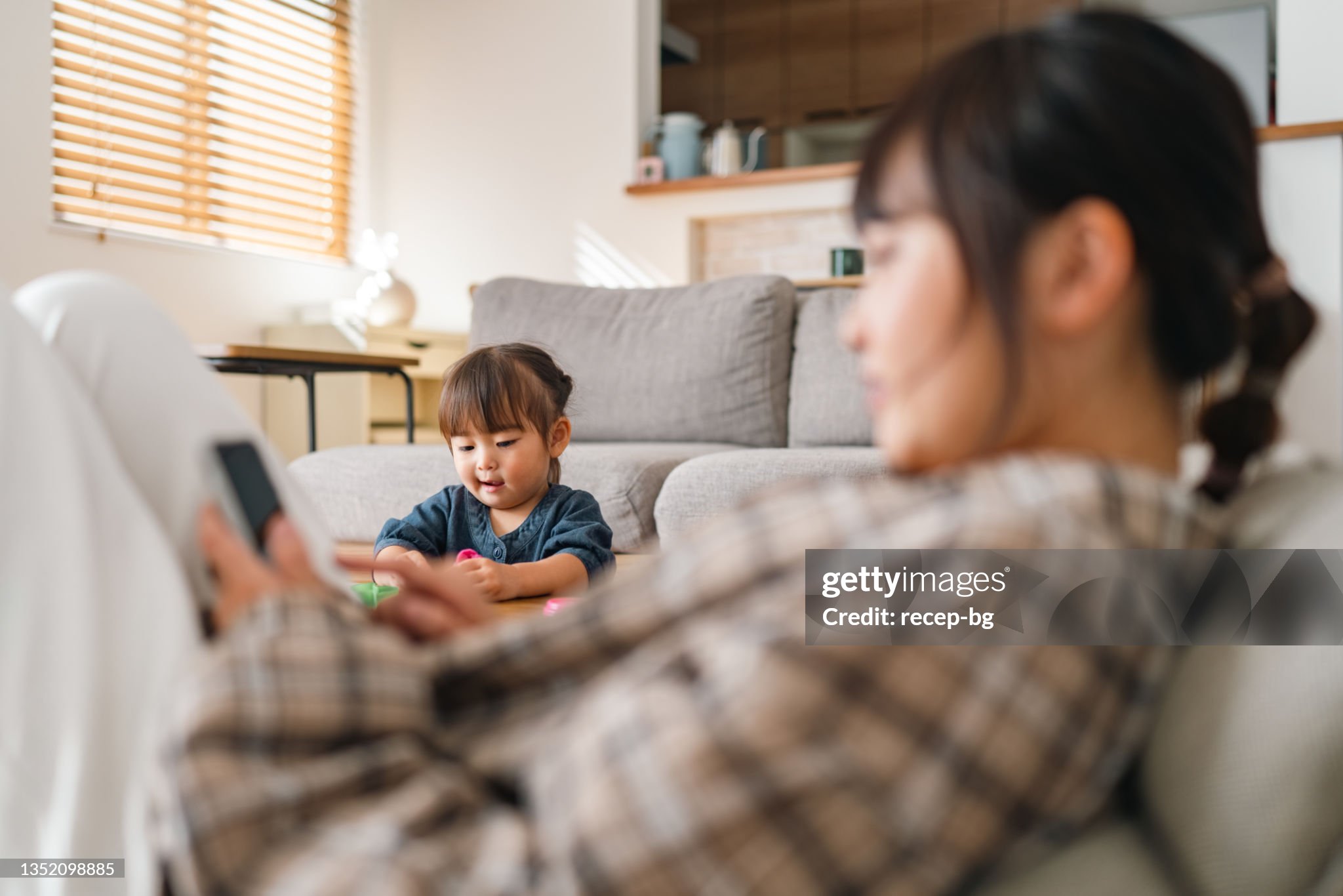 Mother using smart phone with her toddler daughter in the background.